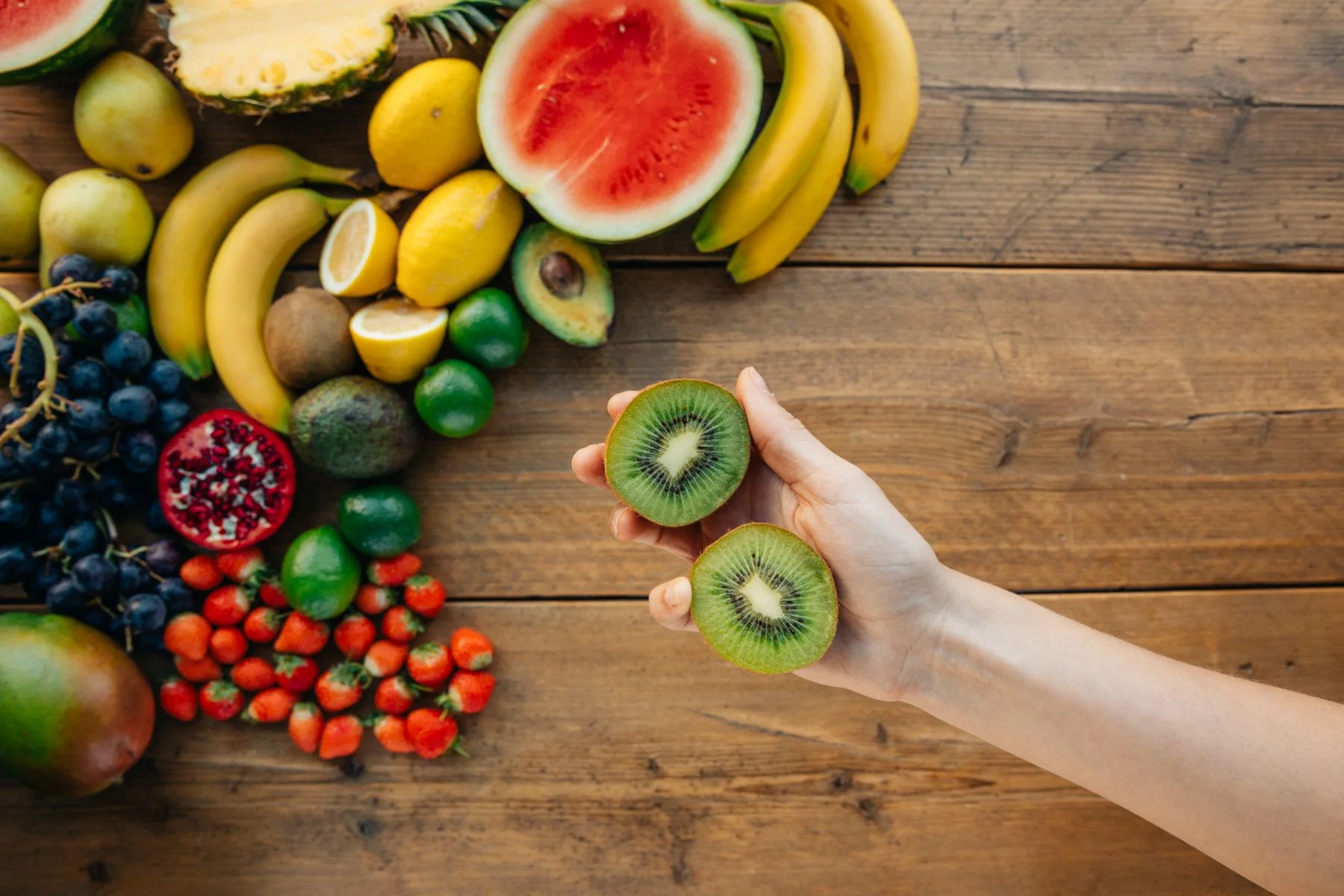 Różne owoce na stole i kiwi w dłoni